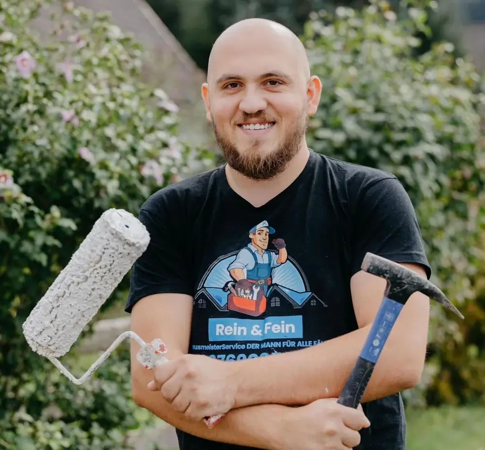 Florian Iballa im Rein & Fein T-Shirt, mit Malerrolle und Hammer im Garten